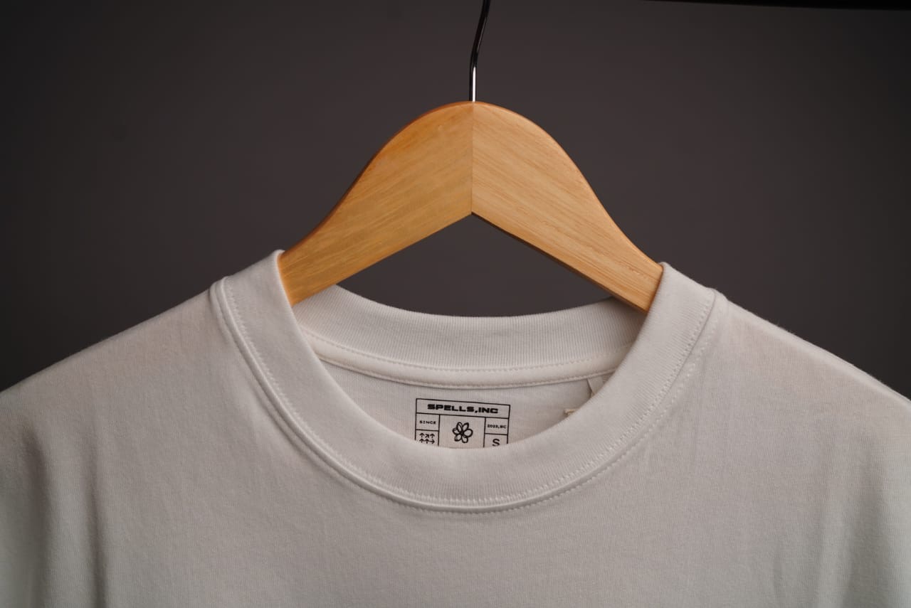 Spells t-shirt on a wooden hanger showing the woven Spells, Inc. neck label